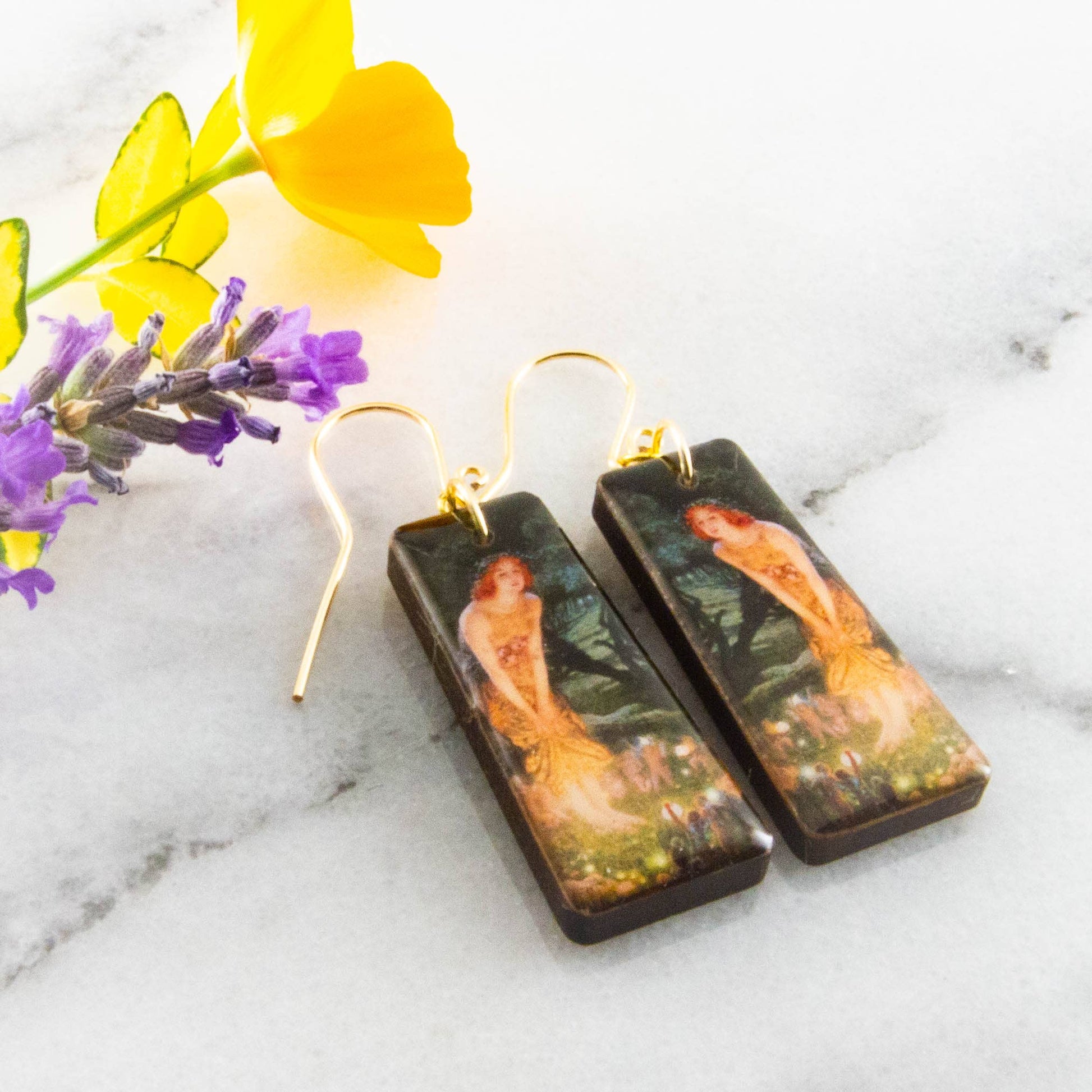 Pair of earrings with artistic design on a marble surface with flowers.