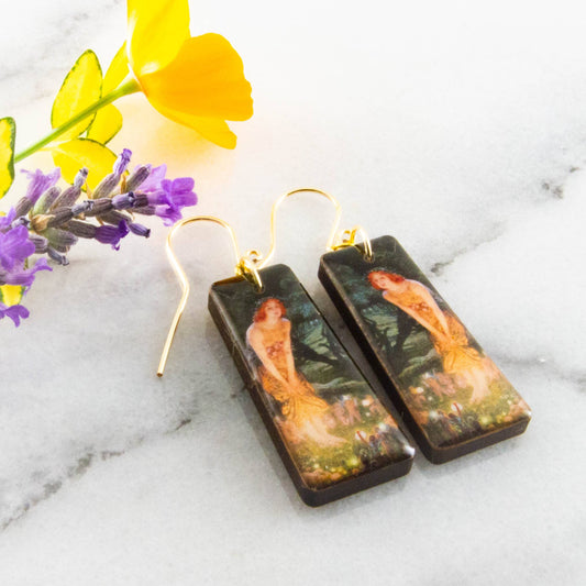 Pair of earrings with artistic design on a marble surface with flowers.