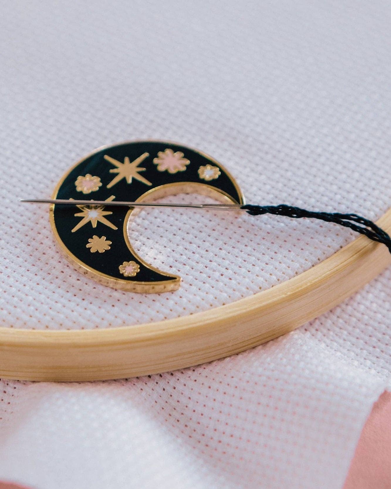 Embroidery hoop with a black and gold embroidered design on a white fabric background