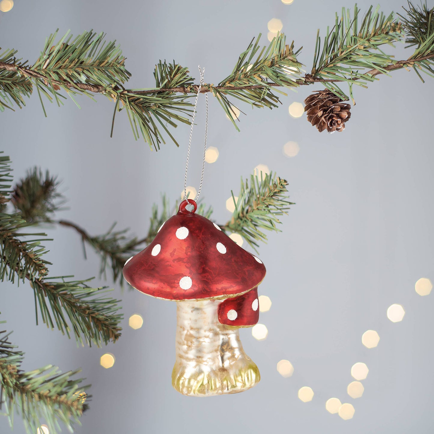 Mushroom-shaped Christmas ornament with red cap and white spots hanging on a tree branch.