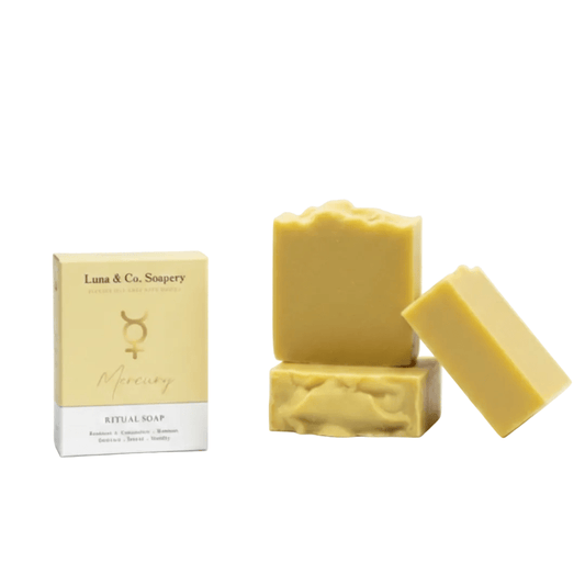 Three bars of pale yellow Mercury Ritual Soap by Luna & Co. Soupery are displayed next to their cream-colored packaging box on a solid white background.