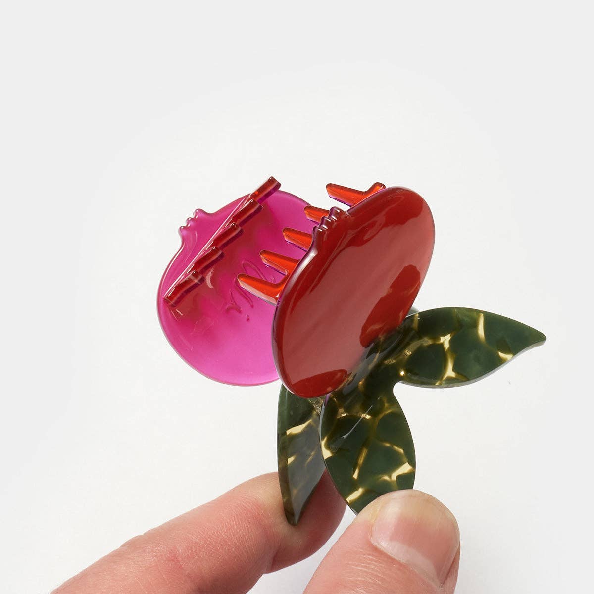 Colorful hair clip with pink and red sections held by a hand on a white background