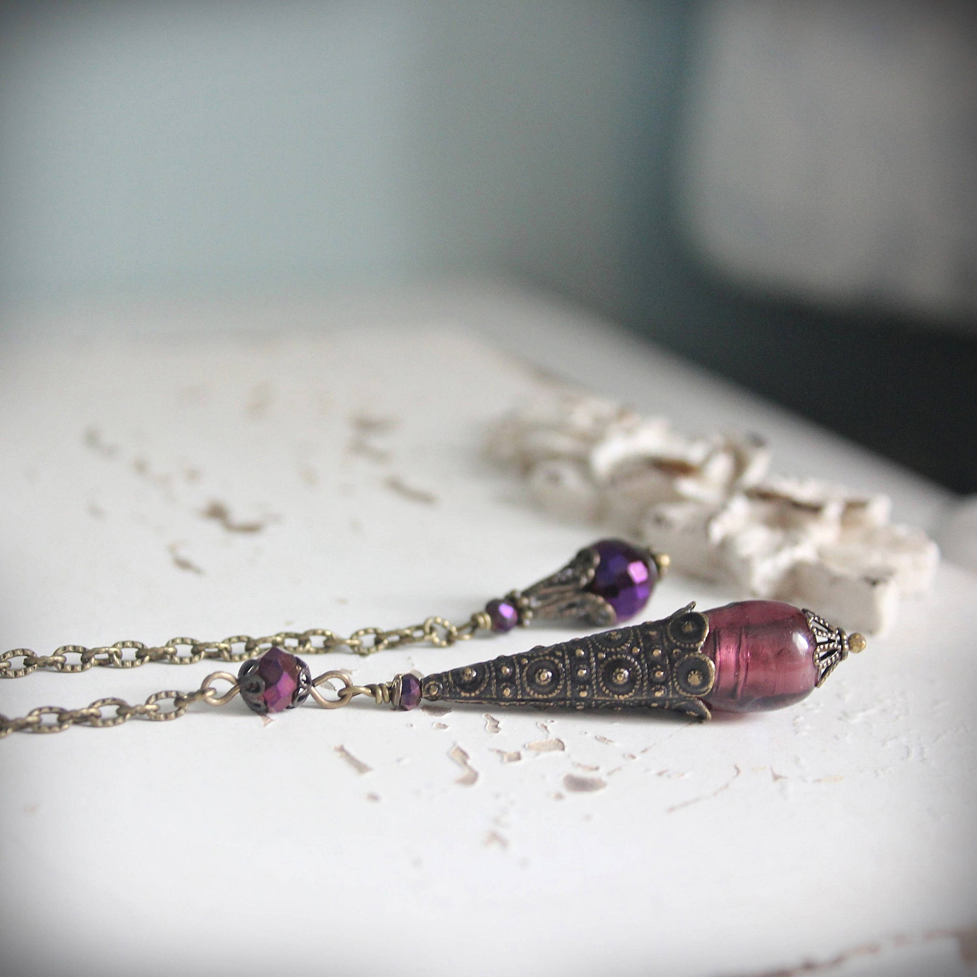 pendulum with purple beads and decorative elements on a light surface