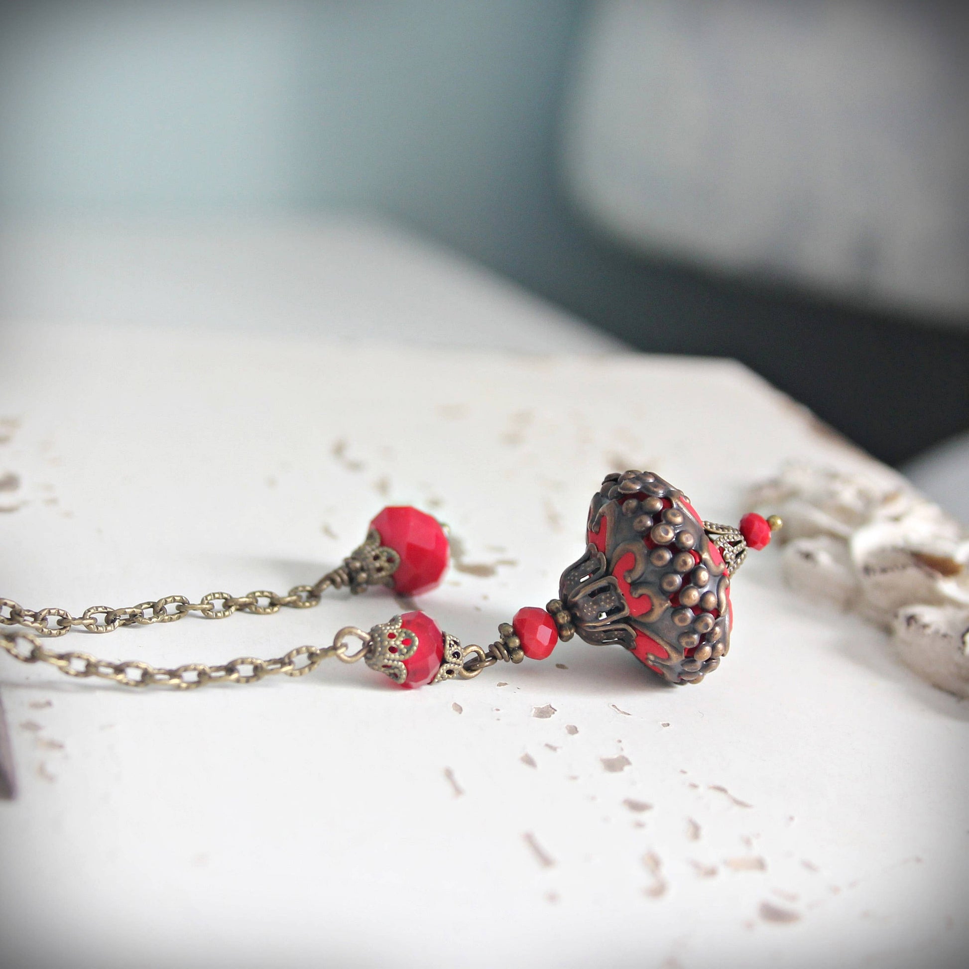 Pendulum with red beads and a decorative clasp on a light surface