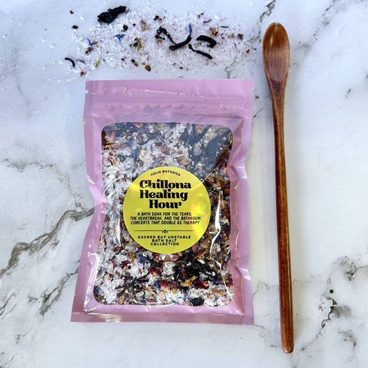 A pink resealable pouch labeled 'Chilpa Healing Hour' by Sacred Earth Vegetables, filled with a multicolored herbal mixture, placed on a white marble surface with a wooden spoon beside it.