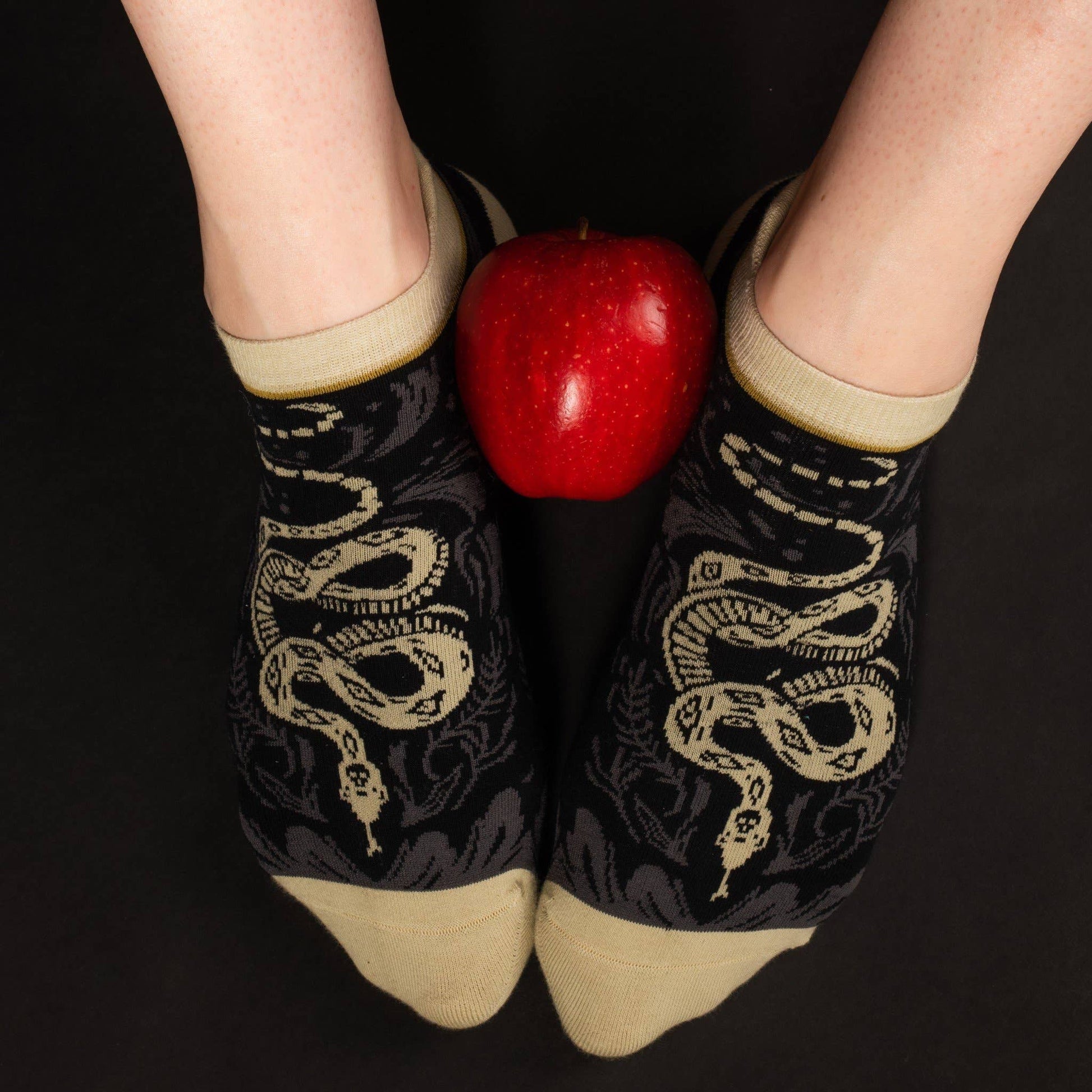 Black socks with snake design held between a red apple on a black background