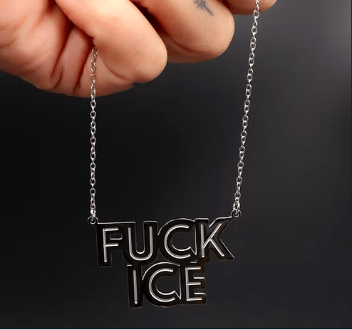 Necklace with 'FUCK ICE' pendant held by a hand against a dark background