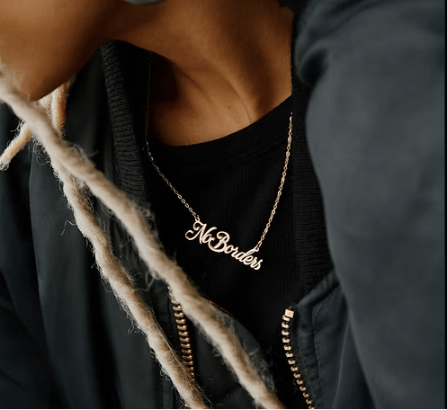 Person wearing a black top with 'No Borders' necklace, blurred background
