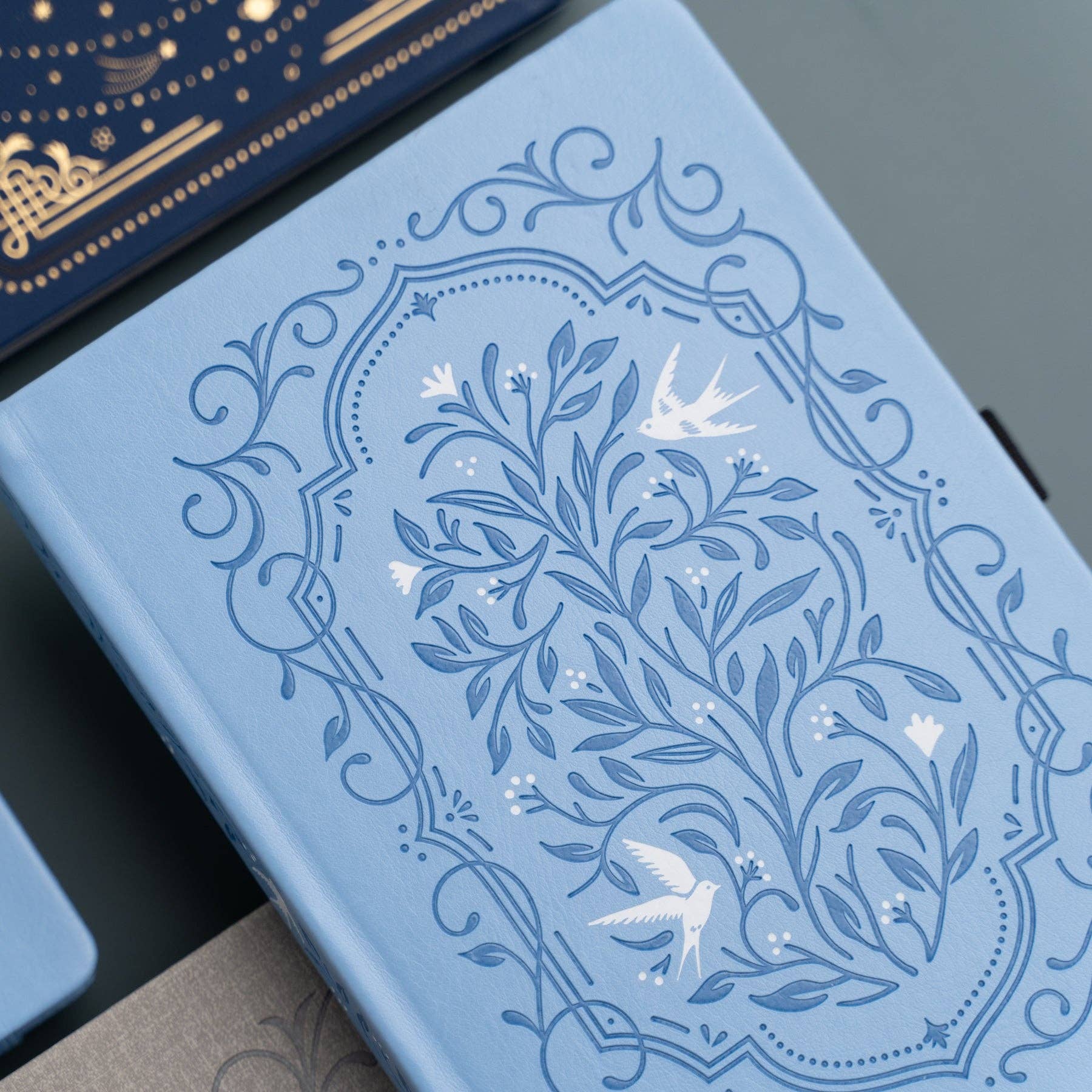 Blue notebook with intricate floral and bird design on a dark surface