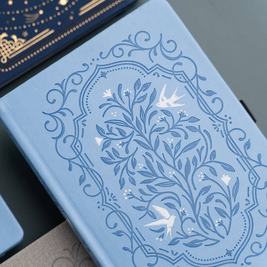 Blue notebook with intricate floral and bird design on a dark surface