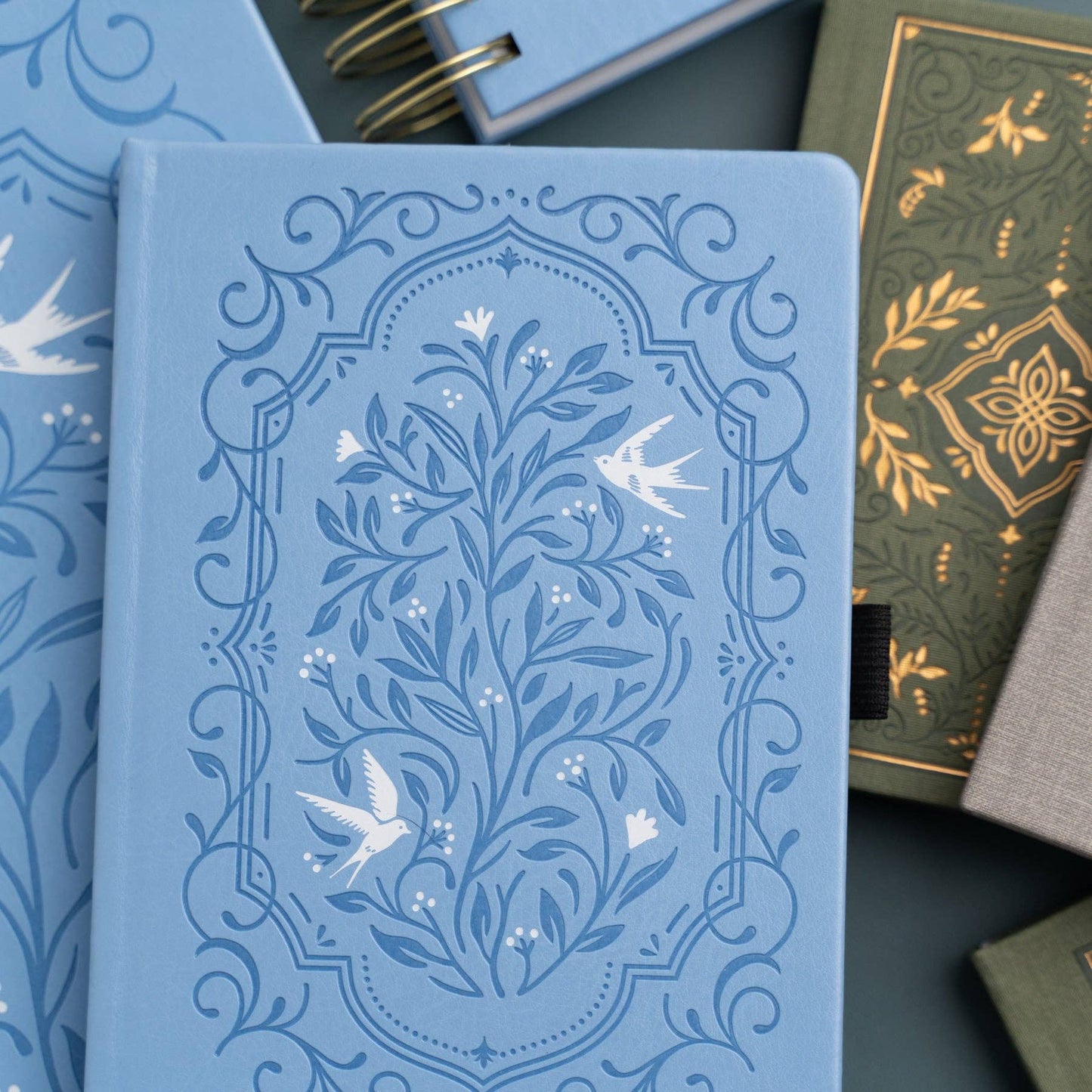 Blue notebook with floral and bird design, surrounded by other notebooks.