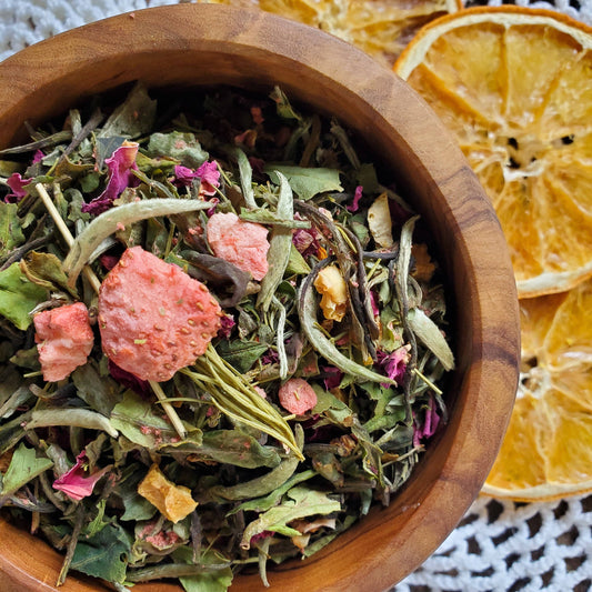 Wooden bowl filled with dried herbs and fruits, with dried oranges in the background.