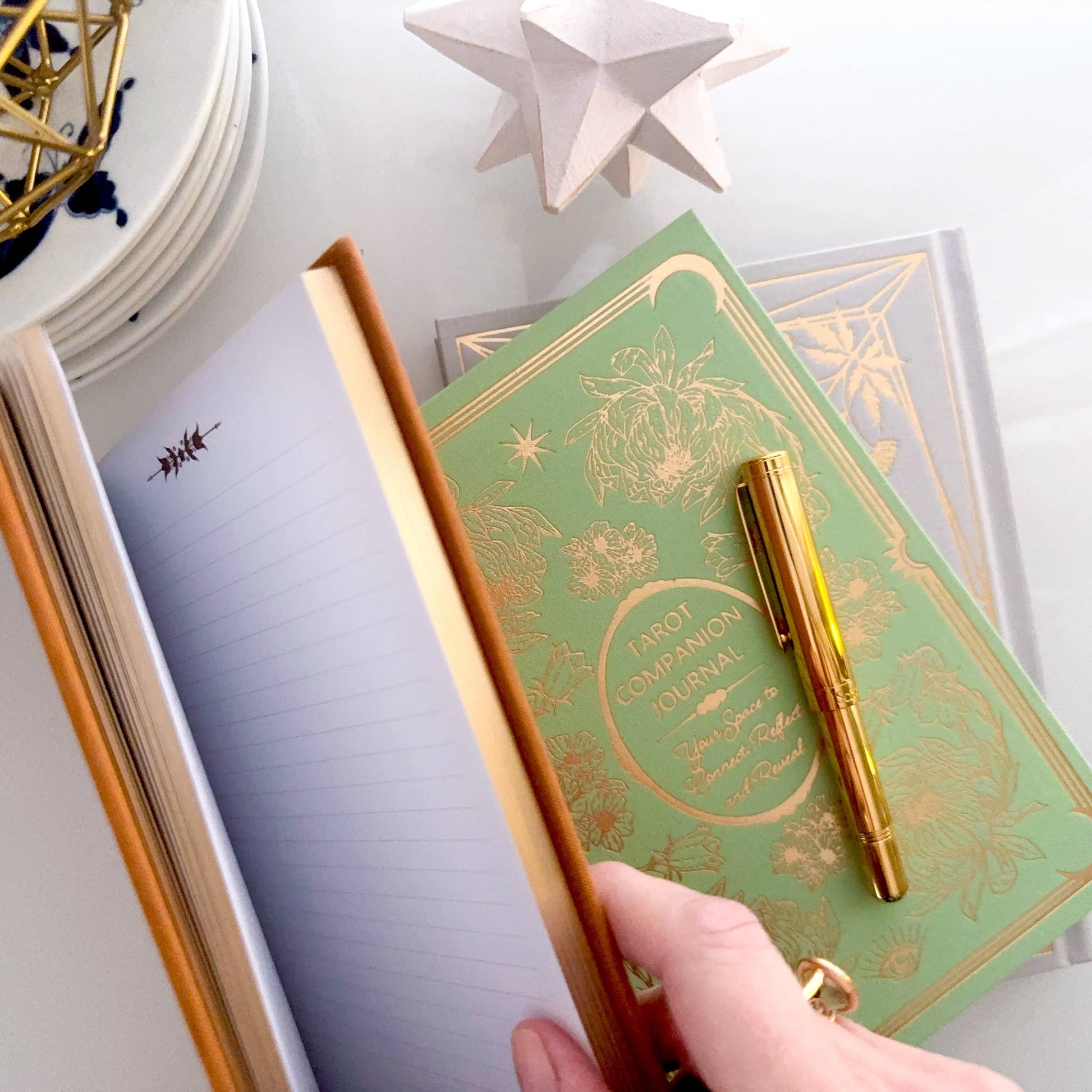 Green notebook with gold design and a gold pen on a white surface