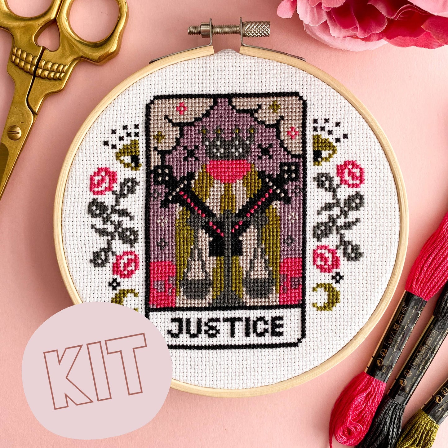 Cross-stitched tarot card design in an embroidery hoop with scissors and thread on a pink background.