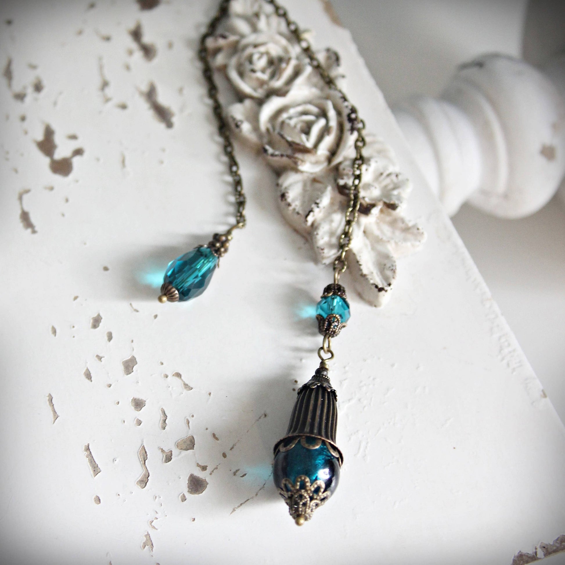 Pendulum with blue beads and decorative elements on a textured white surface