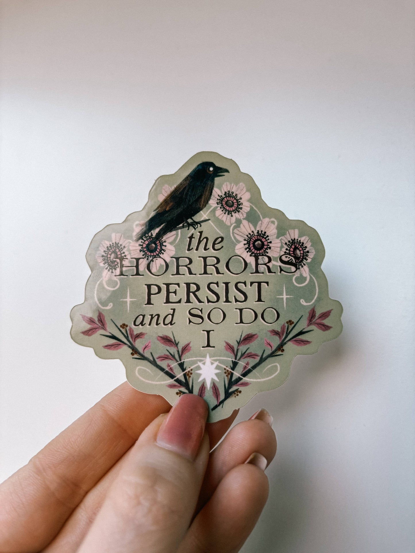 Hand holding a decorative sticker with text and floral design on a plain background