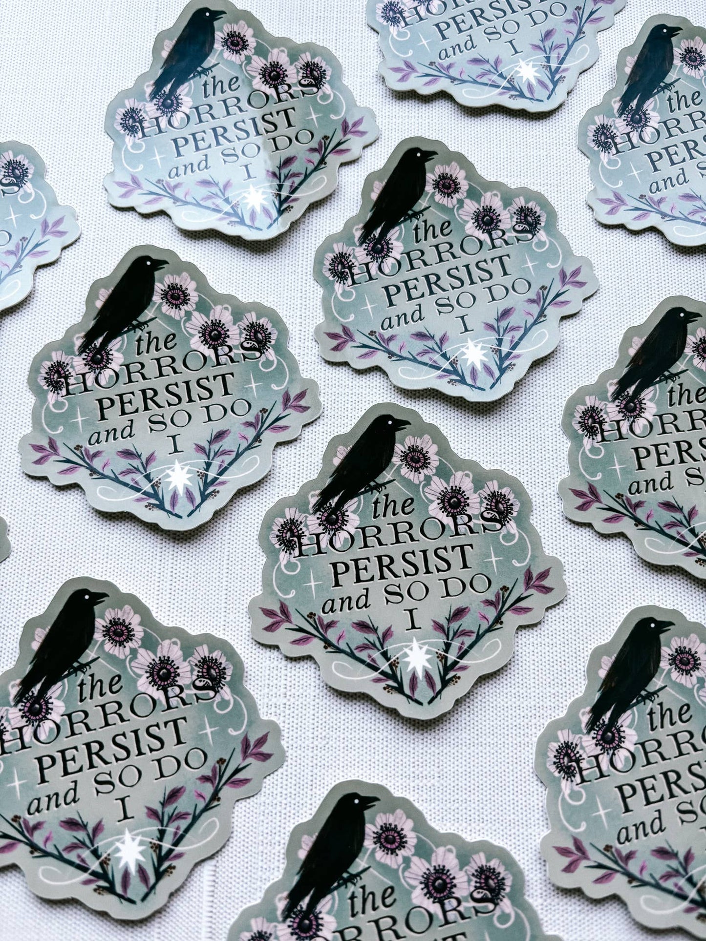 Sticker with text 'The horrors persist and so do I' featuring a black bird and flowers on a light gray background.