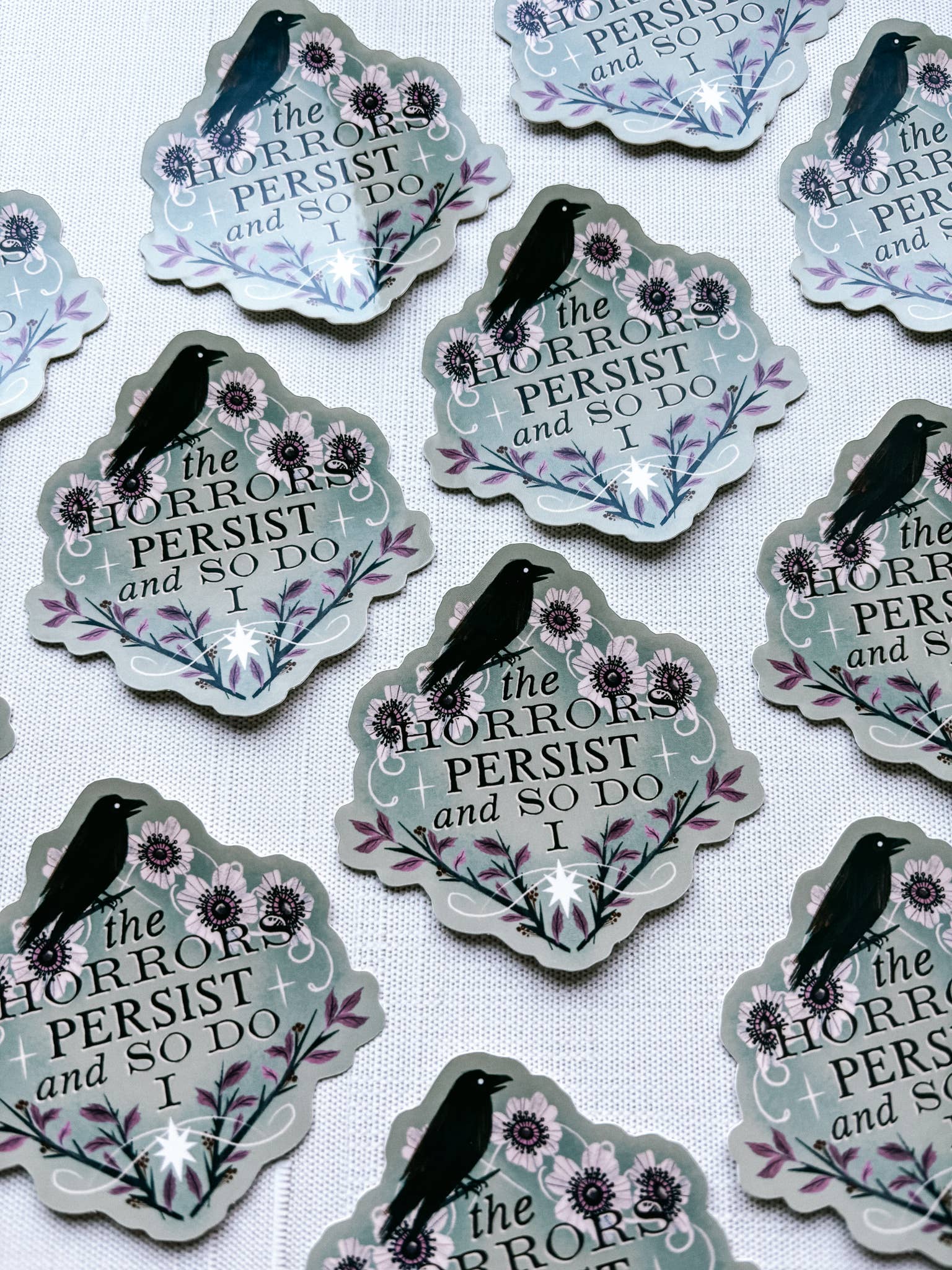 Sticker with text 'The horrors persist and so do I' featuring a black bird and flowers on a light gray background.
