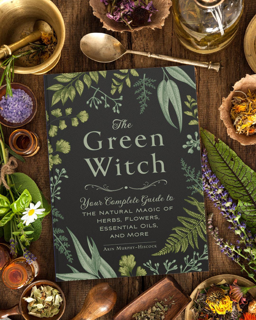 Book titled 'The Green Witch' surrounded by herbs and natural items on a wooden surface