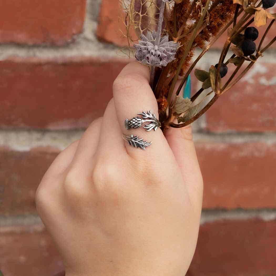 Hand holding dried flowers with silver leaf-shaped rings against a brick wall.