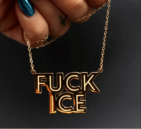 Gold necklace with 'FUCK ICE' pendant held by a hand with blue nail polish against a dark background.