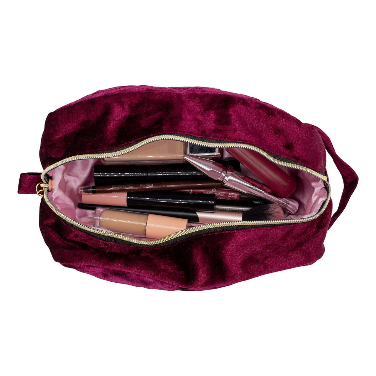 A burgundy velvet makeup bag shown open, revealing a light pink interior lined with various cosmetic items including lipsticks, brushes, and compacts.