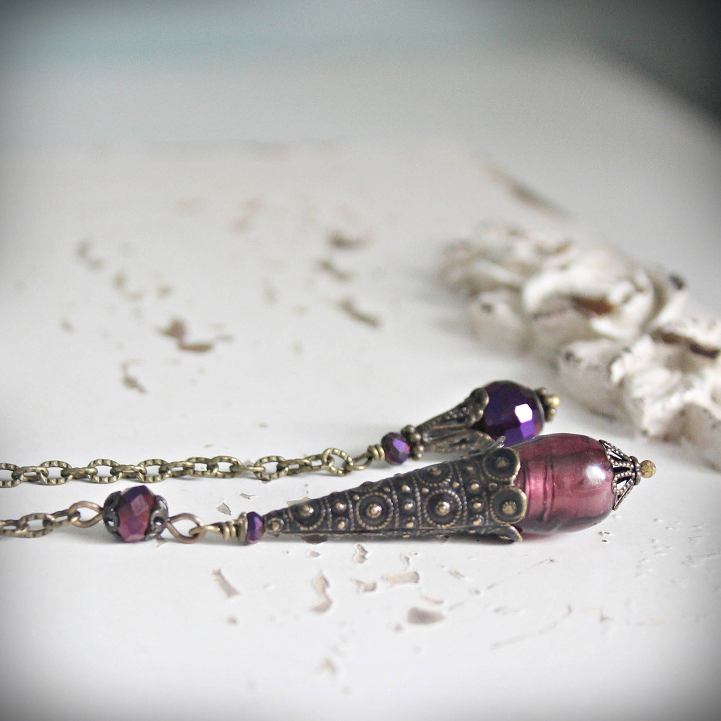 Pendulum with purple beads and decorative clasp on a light background