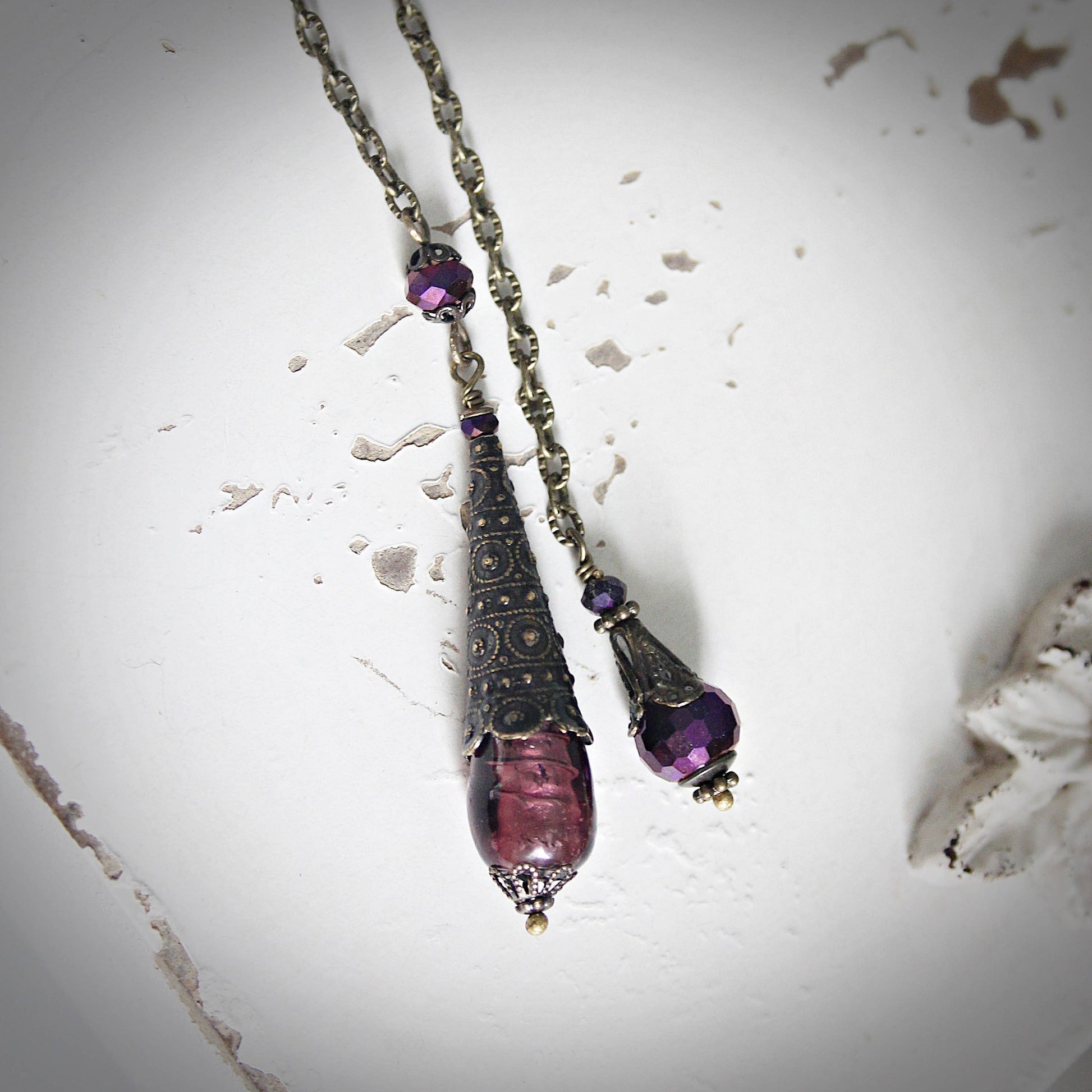 Purple beaded pendulum with decorative elements on a textured white surface