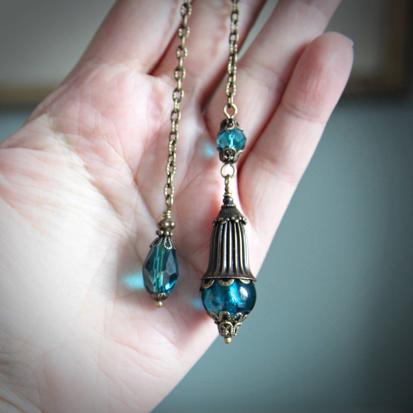 Pendulum with blue beads and gold chain held in a hand against a neutral background