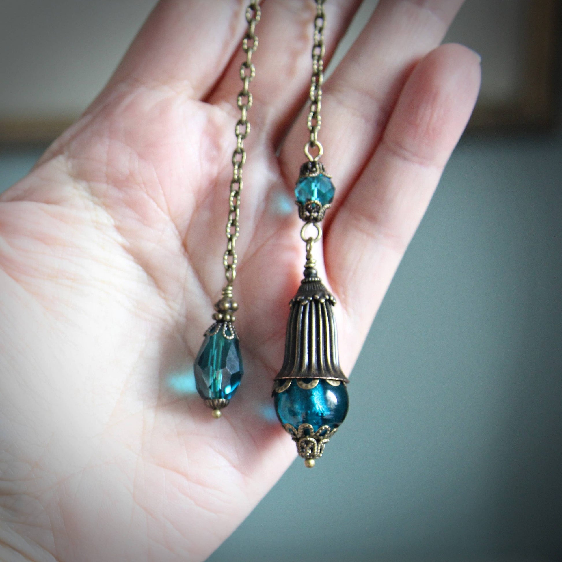 Pendulum with blue beads and gold chain held in a hand against a neutral background