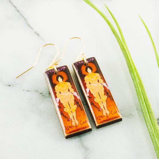 Pair of earrings with artistic designs on a marble surface with grass.