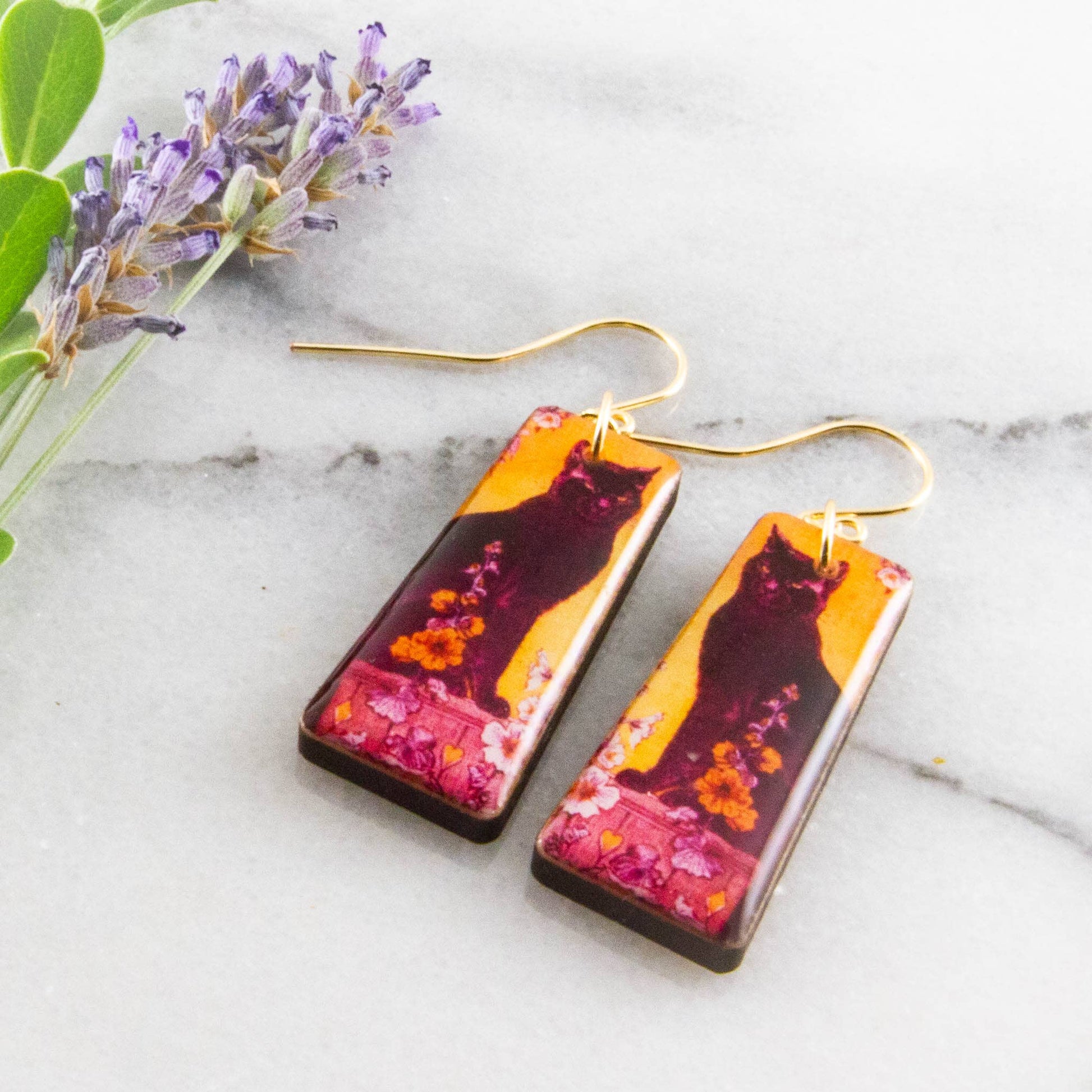 Pair of earrings with a cat design on a marble surface with lavender.