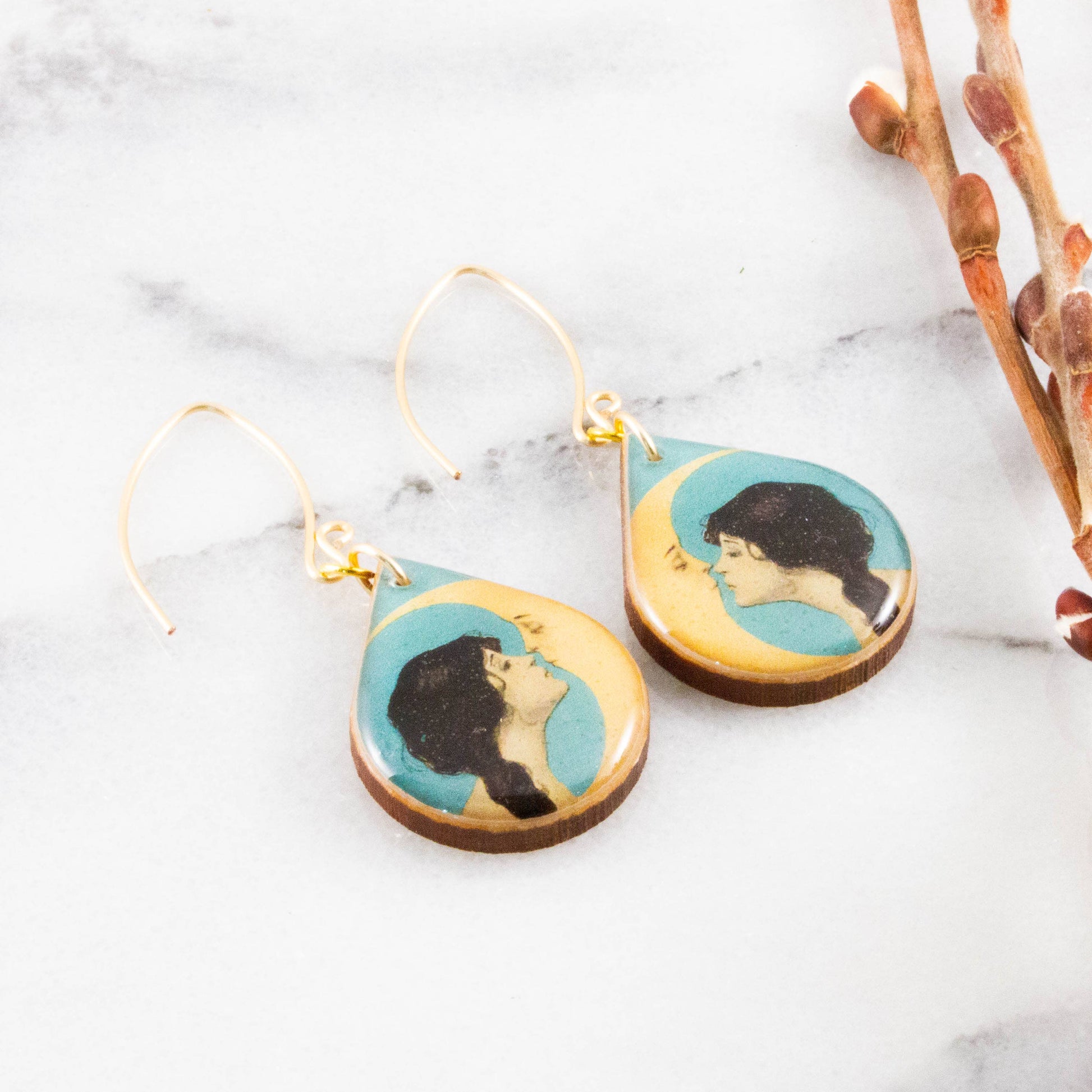 Teardrop-shaped earrings with artistic designs on a marble surface
