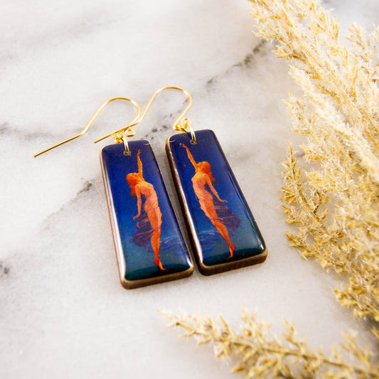 Pair of earrings with artistic design on a marble surface with dried plants.