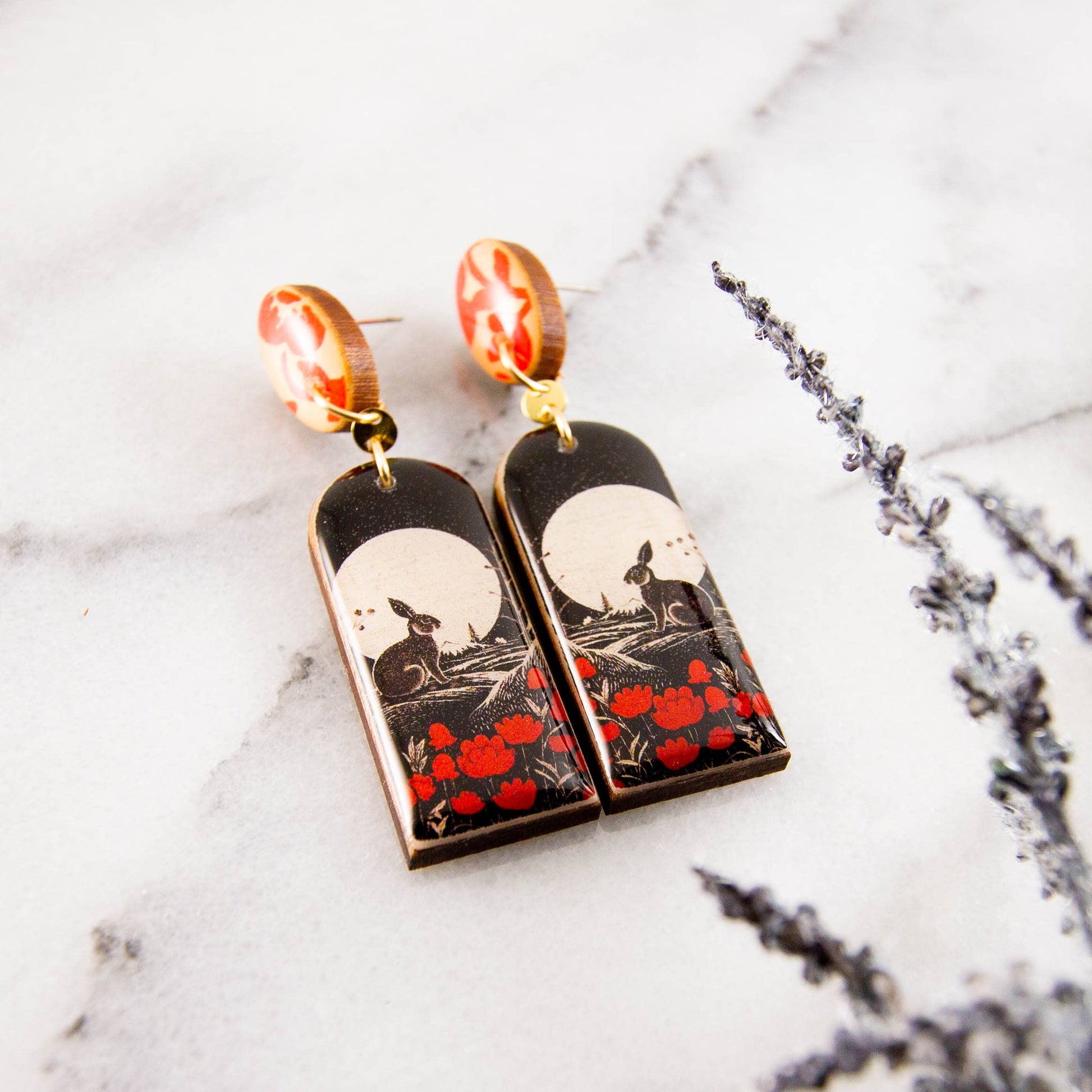 Pair of earrings with rabbit and moon design on a marble surface