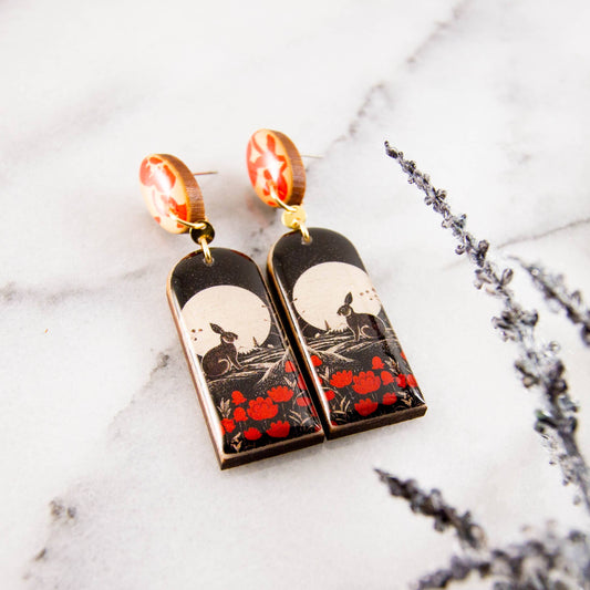 Pair of earrings with rabbit and moon design on a marble surface