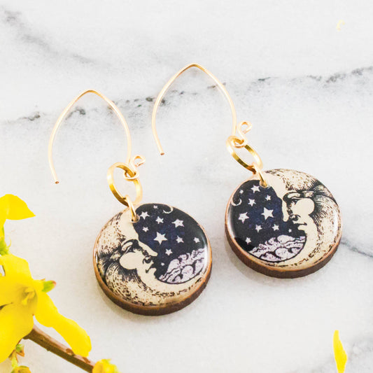 Pair of earrings with celestial design on a marble surface with yellow flowers.