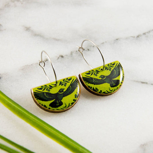 Green and black bird-patterned earrings on a marble surface with green leaves.