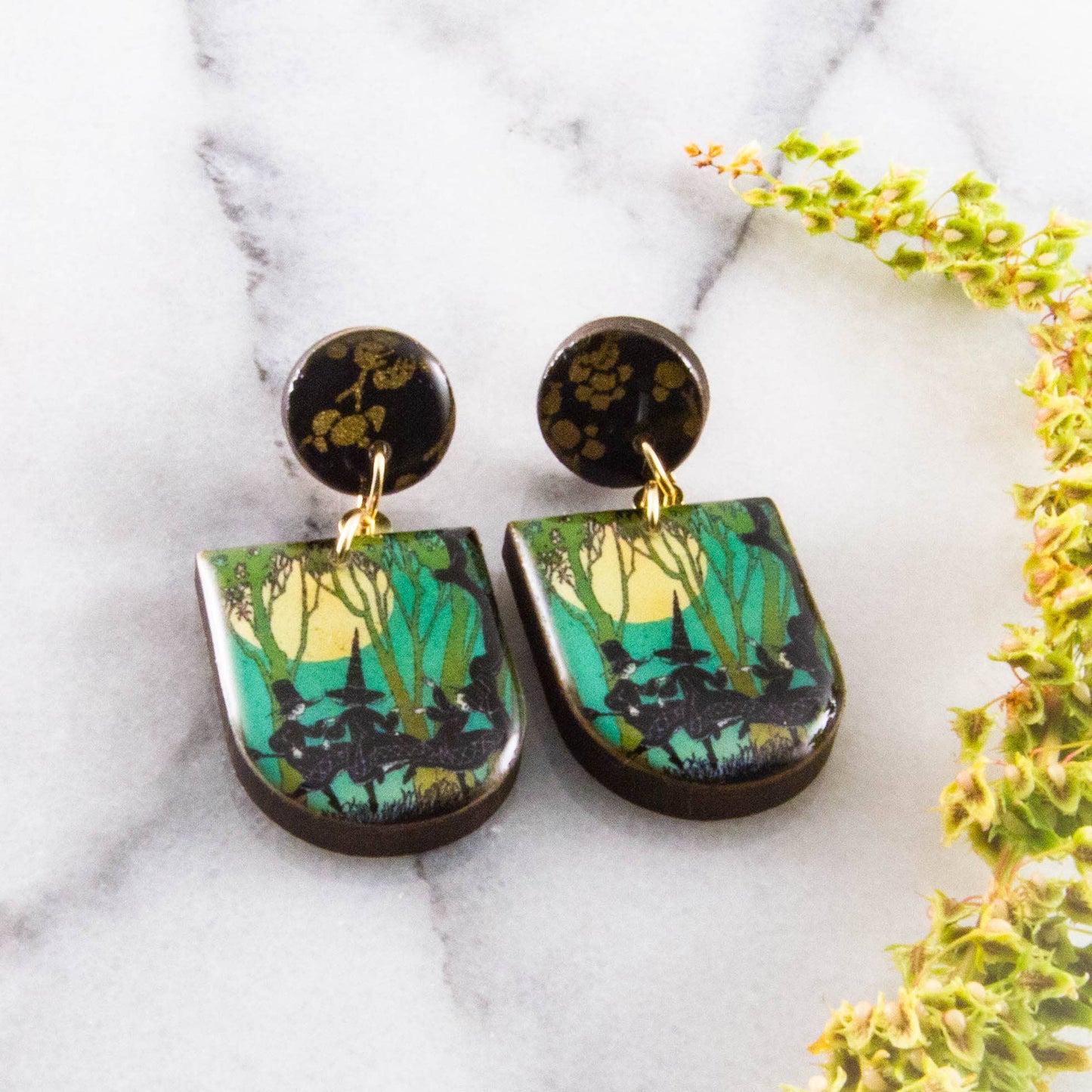Pair of earrings with forest design on a marble surface with flowers.