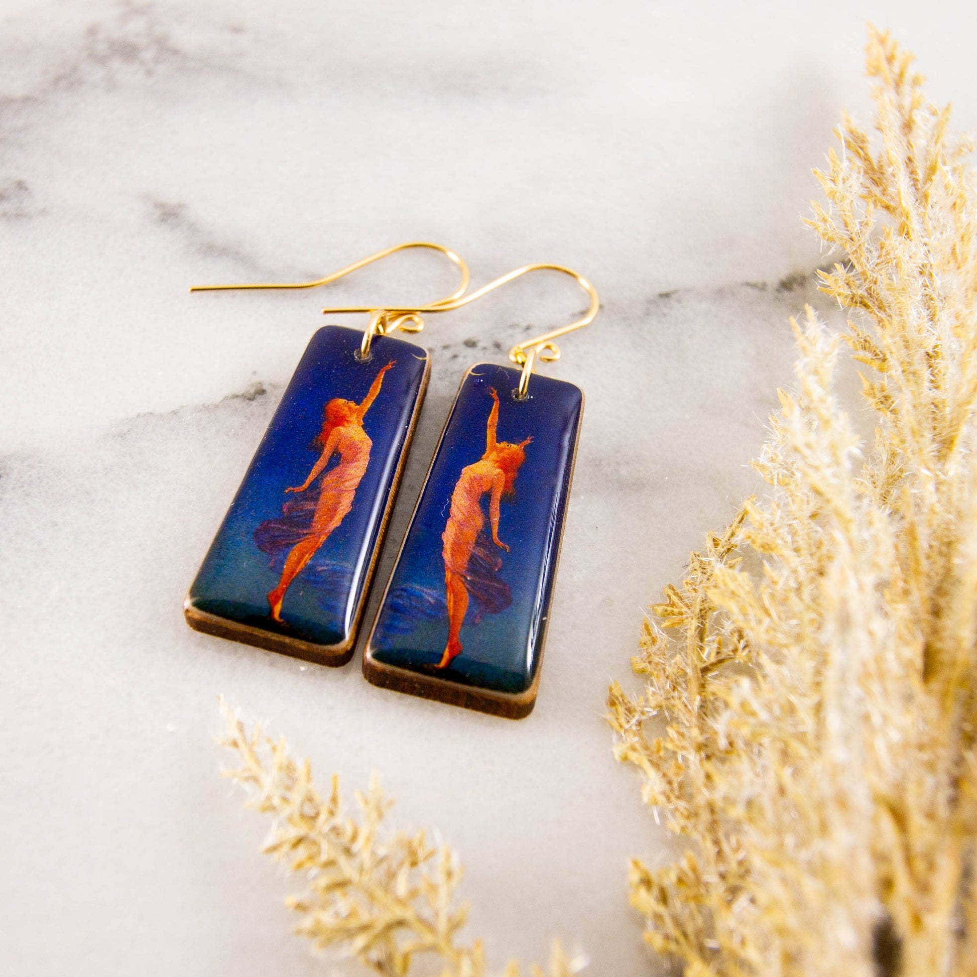 Pair of earrings with artistic design on a marble surface with decorative elements.