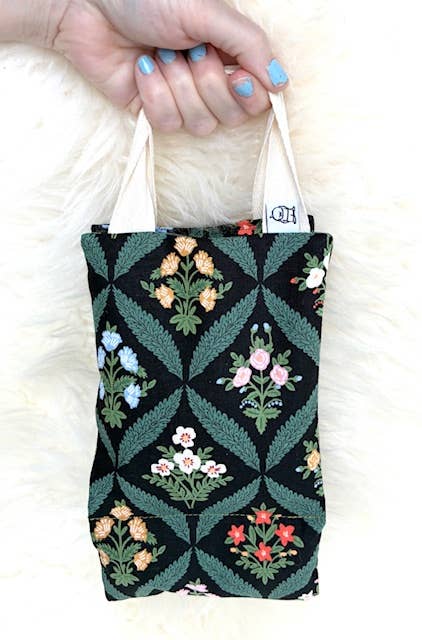 Hand holding a small tote bag with floral pattern on a white background