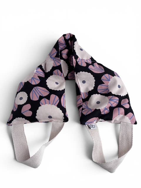 A pair of fabric face masks with a black background and a floral pattern of light pink, lavender, and white flowers, featuring light gray elastic straps.