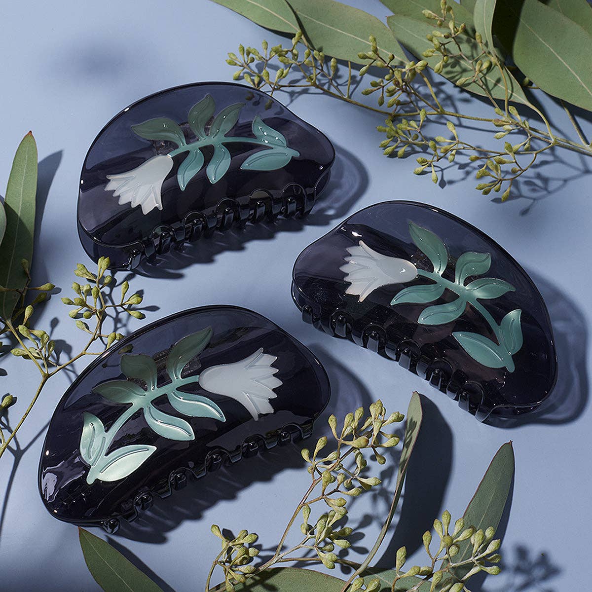Black hair clips with floral designs on a light blue background with green leaves.