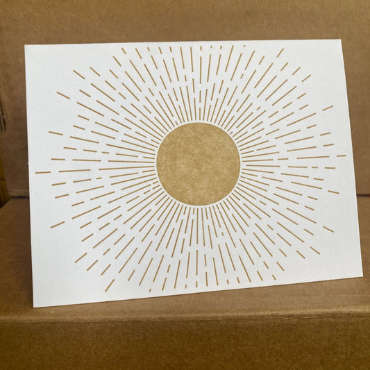 White card with gold sunburst design on a brown background