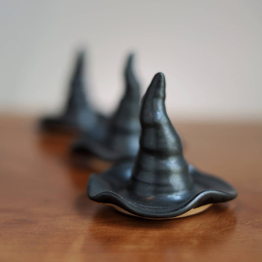 Three small black witch hat-shaped objects arranged in a diagonal row on a wooden surface with a soft-focus neutral background.