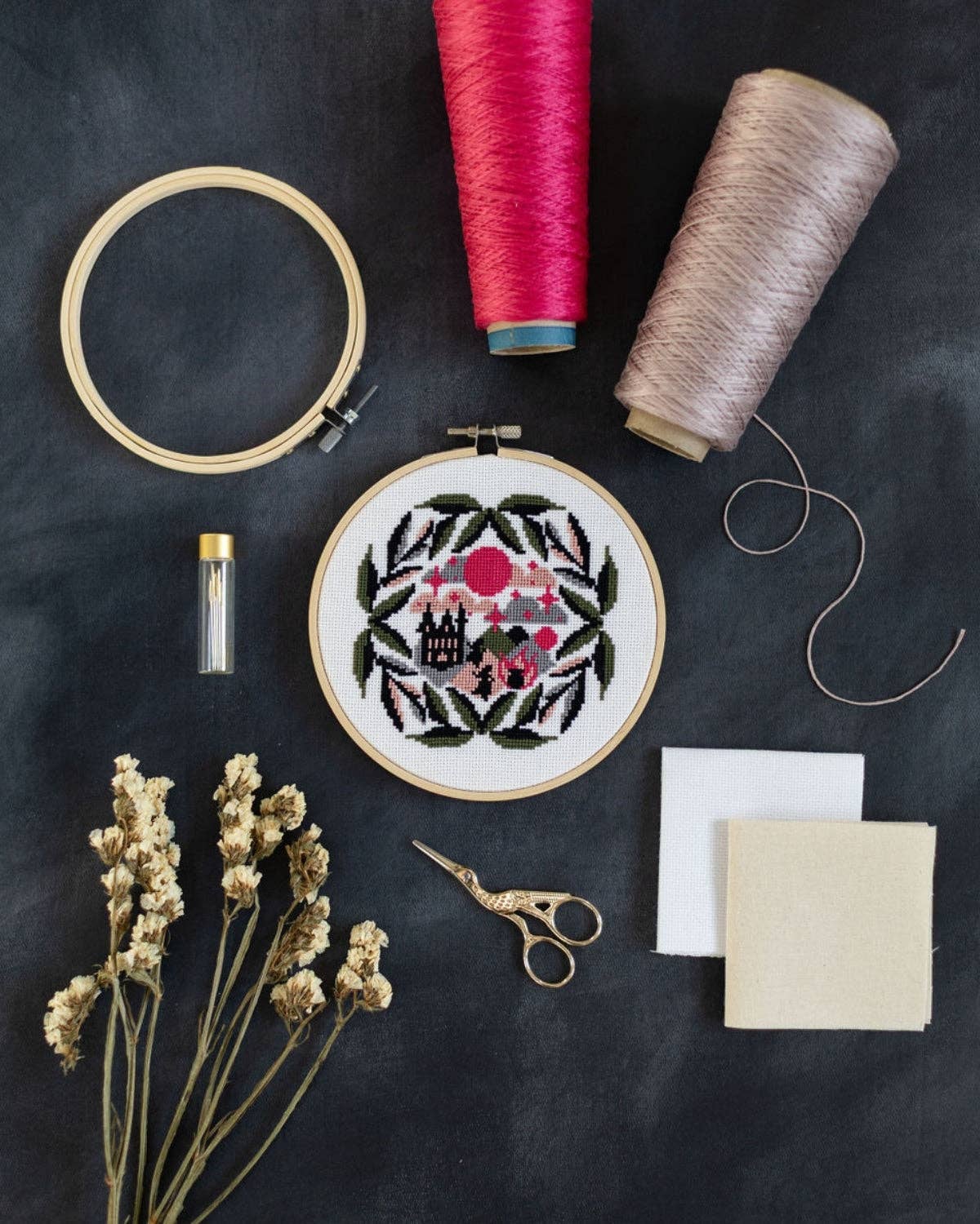 Embroidery hoop with floral design, spools of thread, scissors, and fabric on a dark surface
